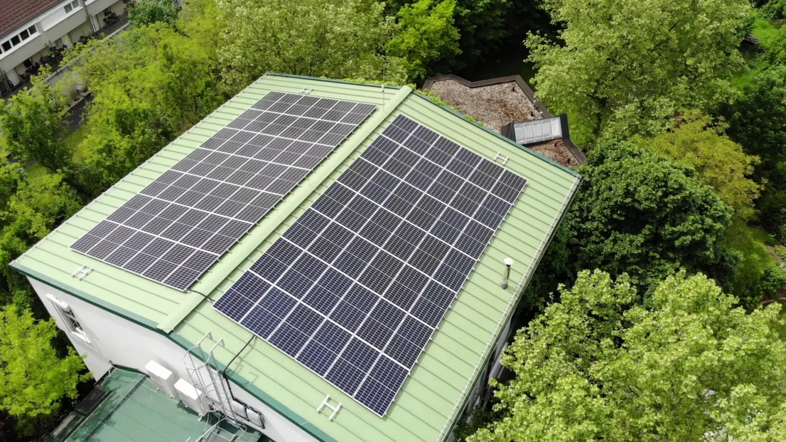 PV-Anlage auf einem Dach mit grüner Deckung, umgeben von Bäumen